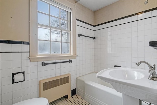 bathroom with radiator heating unit, sink, tile walls, toilet, and a bathing tub