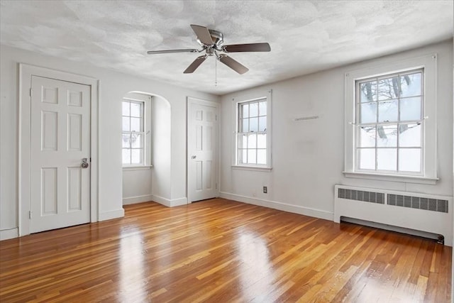 spare room featuring radiator heating unit, a healthy amount of sunlight, light wood-type flooring, and ceiling fan