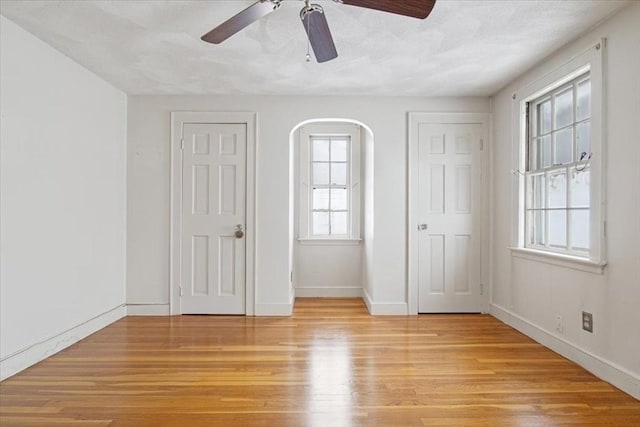 unfurnished bedroom featuring ceiling fan, multiple windows, and light wood-type flooring