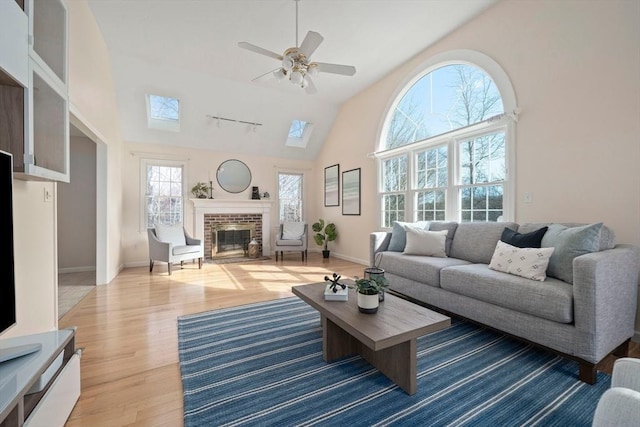 living room with a skylight, rail lighting, a ceiling fan, a brick fireplace, and wood finished floors