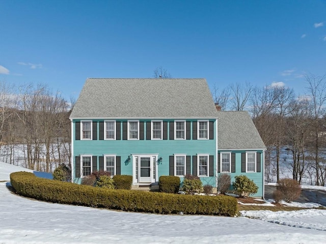 colonial home featuring roof with shingles and a chimney