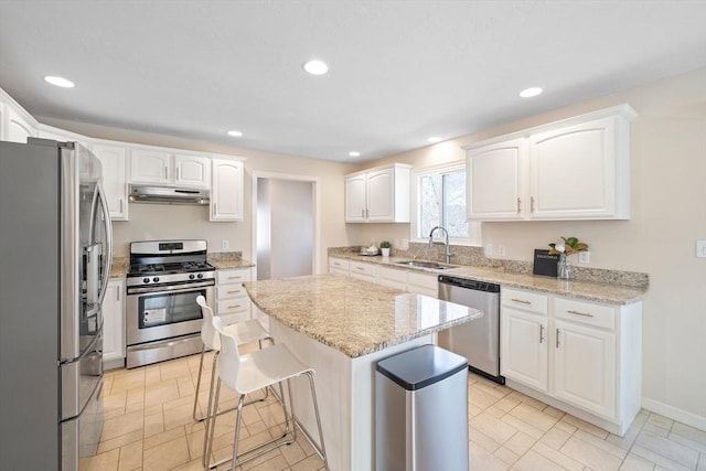 kitchen with stainless steel appliances, white cabinetry, a sink, under cabinet range hood, and a kitchen breakfast bar