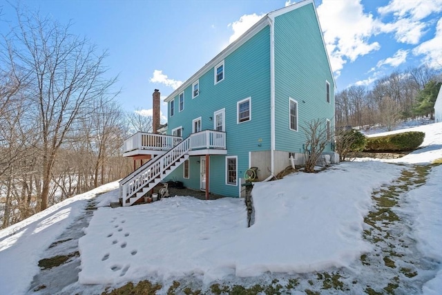 snow covered property with a deck, stairway, and a chimney