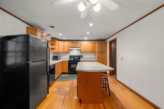 kitchen with light hardwood / wood-style floors, a breakfast bar area, black appliances, and a kitchen island