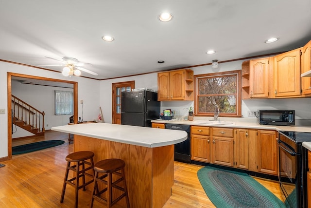 kitchen featuring a center island, black appliances, sink, a breakfast bar, and light wood-type flooring