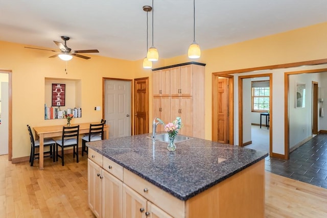 kitchen featuring a ceiling fan, light brown cabinets, baseboards, a sink, and light wood-style flooring