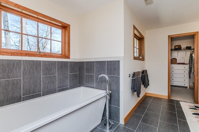 full bath with baseboards, a spacious closet, a soaking tub, and tile patterned flooring