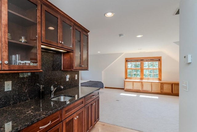 kitchen featuring a sink, dark stone countertops, backsplash, and glass insert cabinets