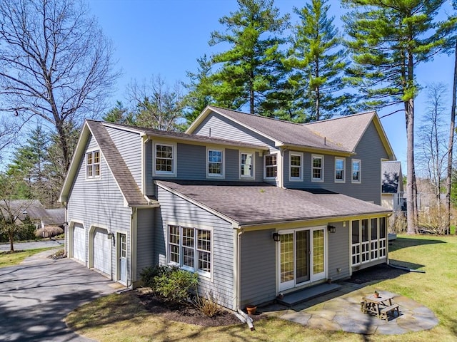 rear view of house featuring roof with shingles, an attached garage, aphalt driveway, a patio area, and a yard