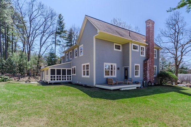 rear view of property featuring a lawn, a chimney, a sunroom, and a wooden deck