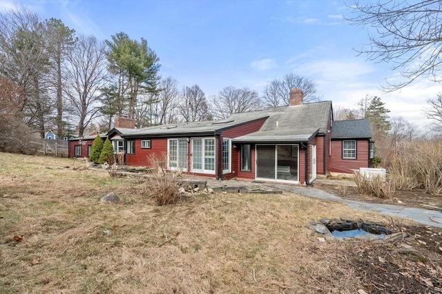 rear view of house with a chimney, a sunroom, and a yard