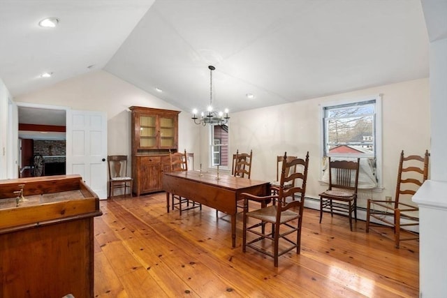 dining area featuring vaulted ceiling, a chandelier, a fireplace, a baseboard radiator, and light wood-style flooring
