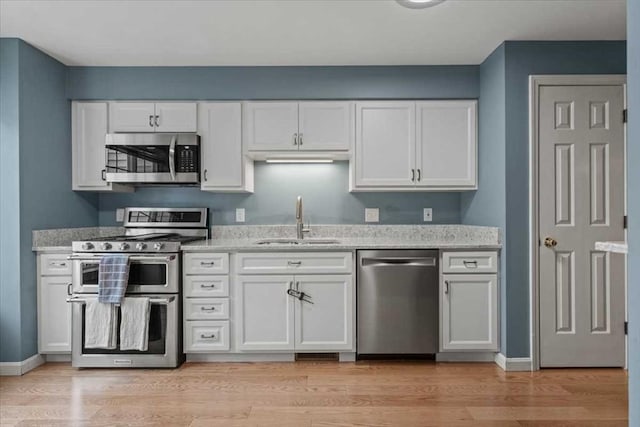 kitchen with stainless steel appliances, a sink, white cabinetry, and light stone countertops