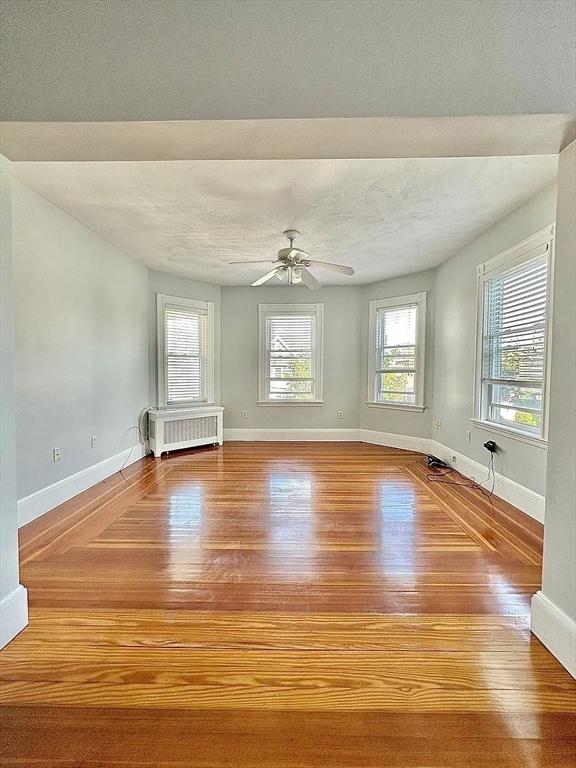 124 Grant Ave, Medford, MA 02155 - unfurnished room with radiator, wood finished floors, healthy amount of natural light, a textured ceiling, and baseboards