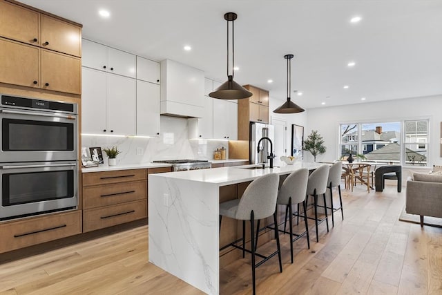 kitchen featuring stainless steel appliances, white cabinets, light hardwood / wood-style floors, an island with sink, and hanging light fixtures