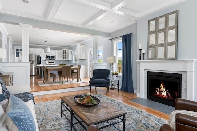 living room featuring coffered ceiling, beam ceiling, light hardwood / wood-style flooring, and ornate columns