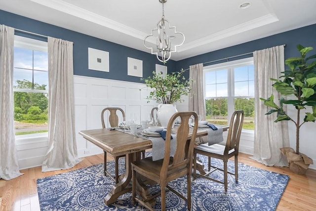 dining area with a notable chandelier, a tray ceiling, a healthy amount of sunlight, and light wood-type flooring