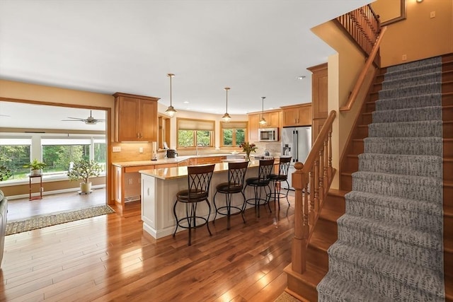 16 Blueberry Way, Webster, MA 01570 - kitchen featuring appliances with stainless steel finishes, light countertops, wood-type flooring, brown cabinetry, and tasteful backsplash