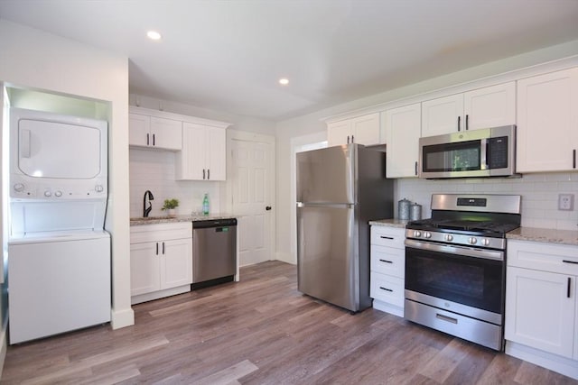 22 Chester Unit 22, Amesbury, MA 01913 - kitchen featuring appliances with stainless steel finishes, stacked washing machine and dryer, backsplash, white cabinets, and light stone counters