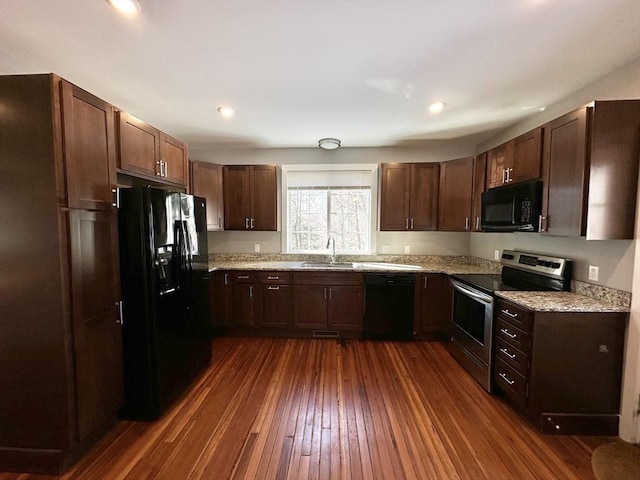 kitchen featuring recessed lighting, dark wood-type flooring, a sink, light stone countertops, and black appliances