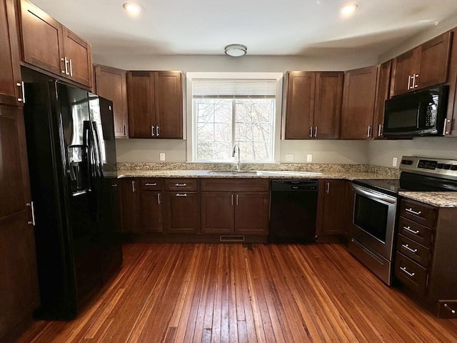 kitchen with dark wood-type flooring, a sink, visible vents, light stone countertops, and black appliances