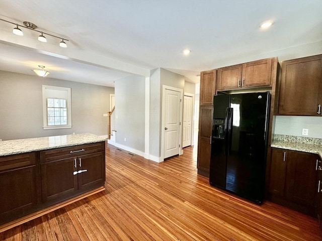 kitchen with black refrigerator with ice dispenser, light wood-style floors, dark brown cabinets, light stone countertops, and baseboards