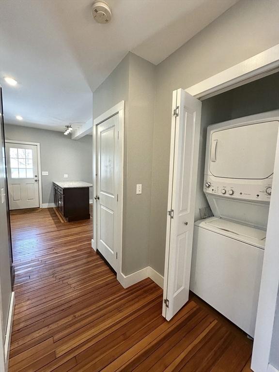 washroom featuring baseboards, laundry area, dark wood-style flooring, and stacked washer / drying machine