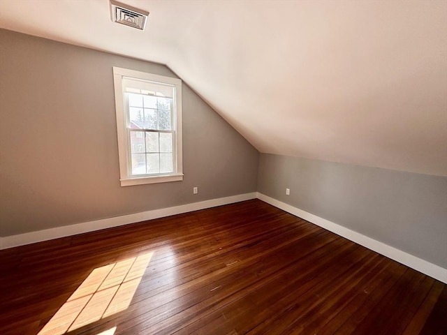 additional living space featuring dark wood-type flooring, visible vents, vaulted ceiling, and baseboards