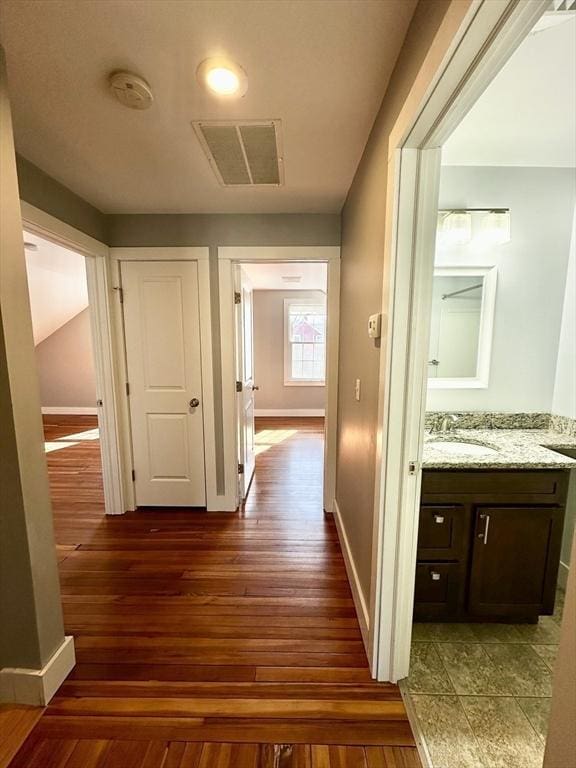 hall featuring baseboards, visible vents, dark wood-type flooring, and a sink