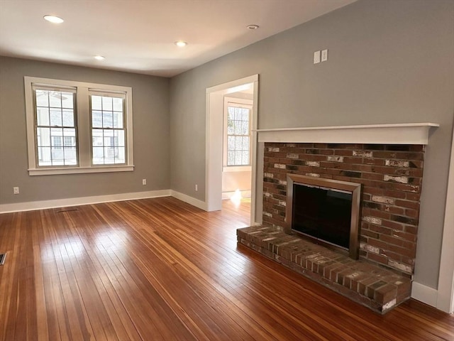 unfurnished living room featuring baseboards, wood-type flooring, and a brick fireplace