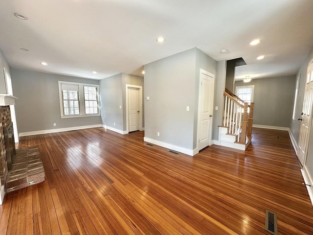 unfurnished living room with baseboards, visible vents, wood-type flooring, stairway, and a fireplace