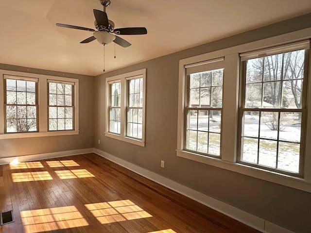 empty room with a ceiling fan, visible vents, dark wood finished floors, and baseboards