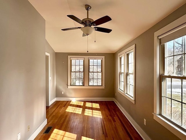 unfurnished room featuring a wealth of natural light, baseboards, visible vents, and dark wood-style flooring