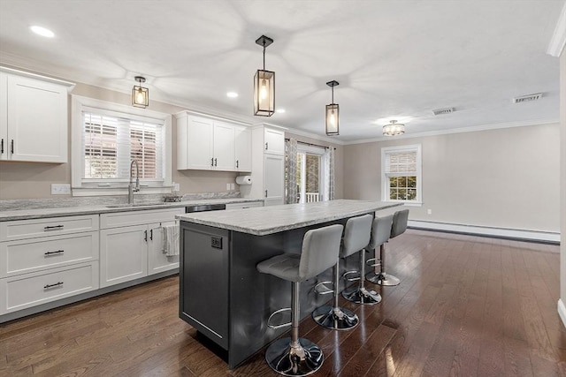 kitchen featuring baseboard heating, hanging light fixtures, a kitchen island, white cabinets, and sink