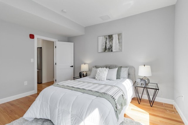 bedroom featuring baseboards, light wood-style floors, and freestanding refrigerator