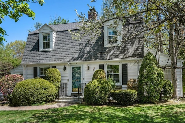 view of front of property with a chimney, a gambrel roof, a shingled roof, and a front lawn