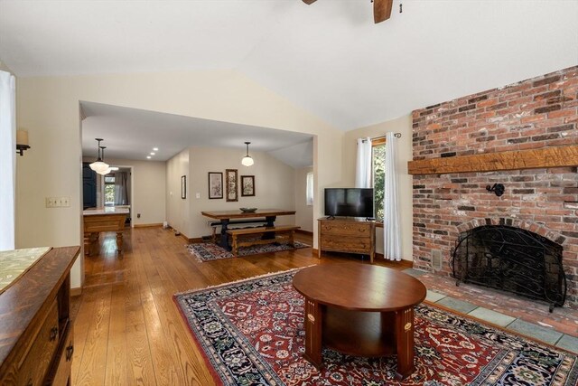 living area with ceiling fan, a brick fireplace, light wood-type flooring, baseboards, and lofted ceiling