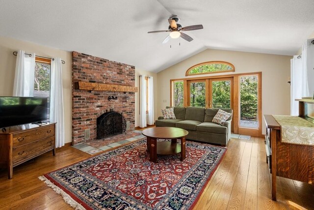 living room featuring light wood-style floors, ceiling fan, vaulted ceiling, and a brick fireplace