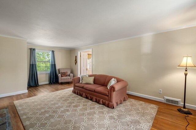 living room featuring visible vents, ornamental molding, baseboards, and wood finished floors