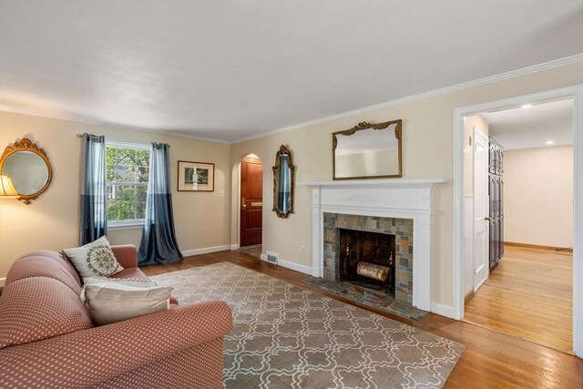 living room with a fireplace, light wood-style floors, arched walkways, baseboards, and visible vents