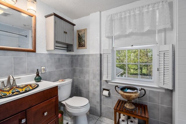 bathroom with a textured ceiling, tile walls, tile patterned floors, vanity, and toilet