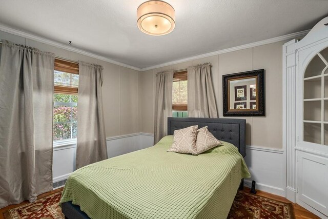 bedroom with ornamental molding, a decorative wall, and wood finished floors