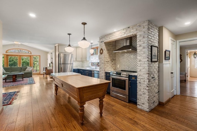 kitchen with blue cabinets, appliances with stainless steel finishes, wall chimney range hood, and hardwood / wood-style flooring