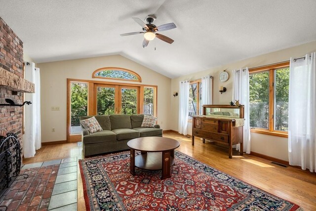 living area featuring ceiling fan, a fireplace, baseboards, vaulted ceiling, and visible vents