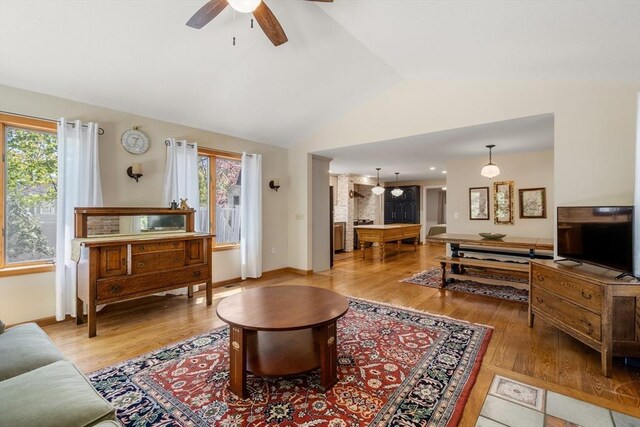 living area with a healthy amount of sunlight, ceiling fan, light wood-type flooring, and lofted ceiling