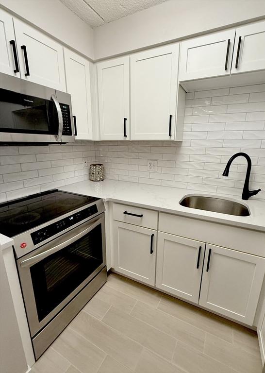 180 Green St Unit 415, Melrose, MA 02176 - kitchen featuring stainless steel appliances, white cabinets, tasteful backsplash, and a textured ceiling