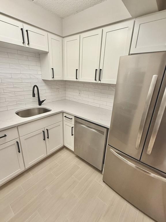 180 Green St Unit 415, Melrose, MA 02176 - kitchen with appliances with stainless steel finishes, light countertops, white cabinetry, tasteful backsplash, and a textured ceiling