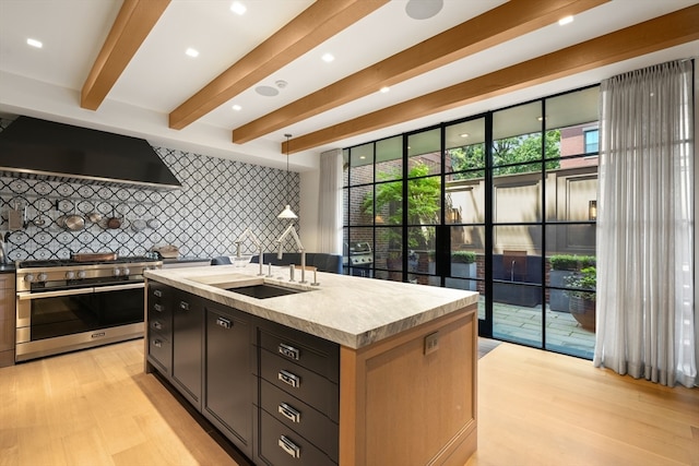 kitchen with high end stove, light hardwood / wood-style floors, an island with sink, wall chimney range hood, and backsplash