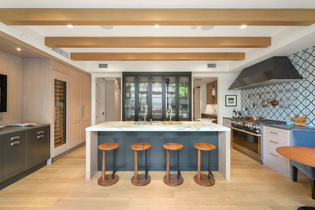 kitchen with a large island, wall chimney range hood, high end stainless steel range oven, a kitchen bar, and decorative backsplash