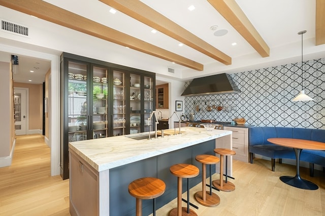 kitchen featuring a breakfast bar area, a center island with sink, wall chimney range hood, and light hardwood / wood-style flooring